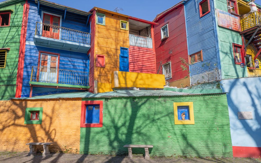 Casas de chapa pintadas de azul, vermelho, amarelo e verde no Caminito, em La Boca, sob céu azul