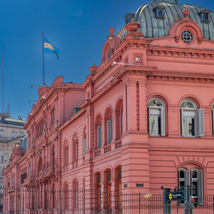 Fachada rosa da Casa Rosada, com cúpula de zinco e a bandeira argentina, sob céu azul