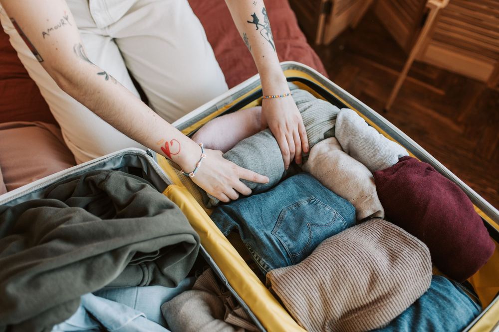 Mãos organizando roupas dobradas dentro de uma mala aberta