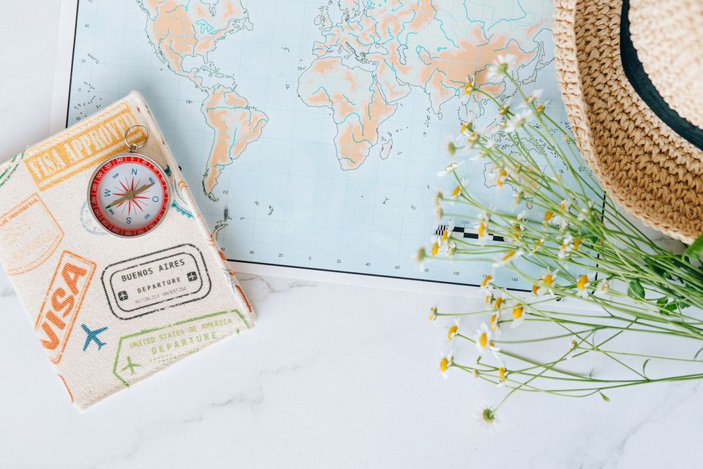Passaporte decorativo de carimbos e bússola sobre mapa do mundo, com flores e chapéu de palha