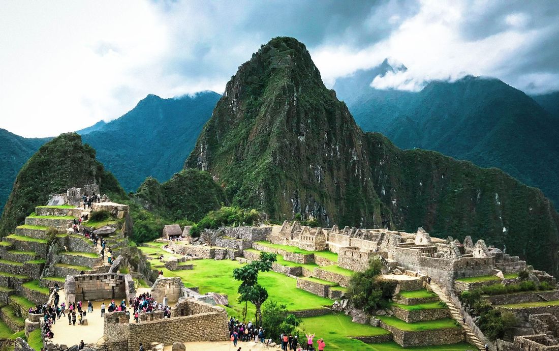 A cidade inca de Machu Picchu, com terraços verdes e a montanha ao fundo, entre nuvens
