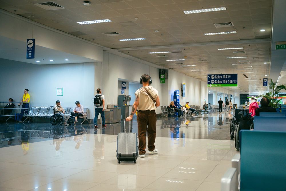 Corredor claro de aeroporto com viajante puxando mala de rodinhas e salas de espera ao fundo