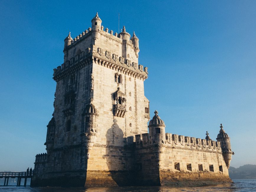 A Torre de Belém, de pedra clara e com ameias, erguida à beira do rio Tejo, contra um céu azul
