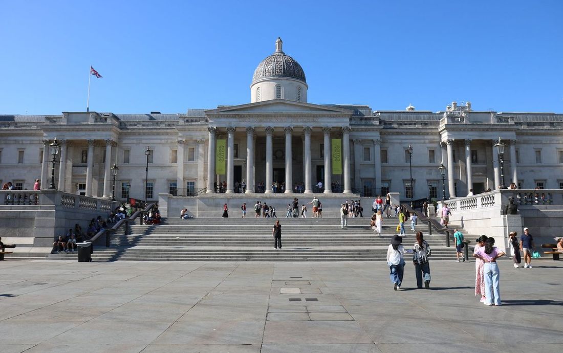 Fachada da National Gallery, com colunas e cúpula, vista da escadaria da Trafalgar Square, sob céu azul