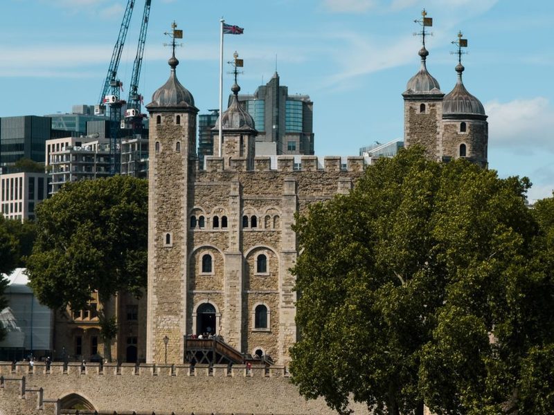 A Torre Branca da Torre de Londres, fortaleza de pedra com torreões, vista do outro lado do rio, com árvores ao lado