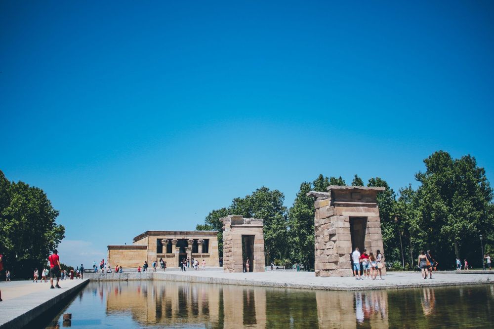 Templo de Debod refletido na água de um lago, em Madri, com pessoas passeando ao fundo