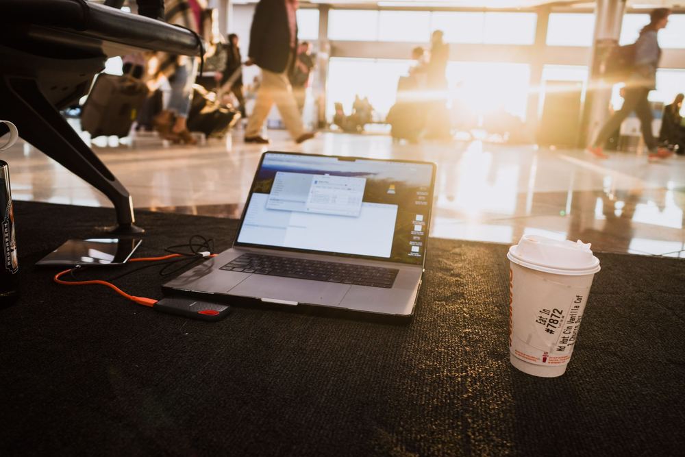 Notebook aberto sobre uma mesa de aeroporto, com copo de café e luz dourada ao fundo