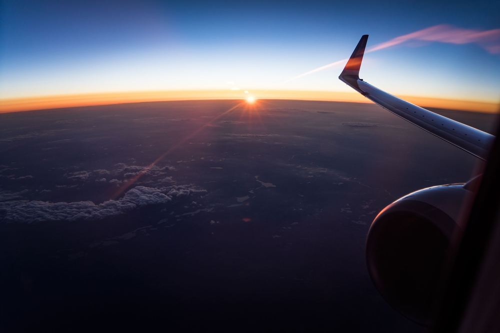 Pôr do sol visto da janela do avião, com asa, motor e horizonte alaranjado