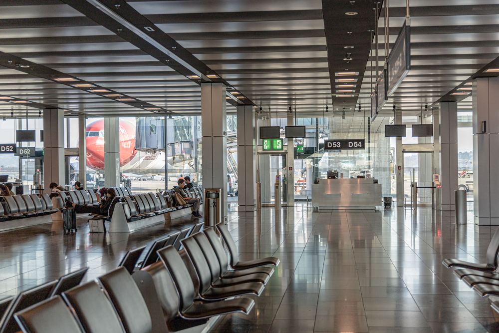 Saguão amplo de aeroporto com fileiras de assentos vazios e luz natural entrando pelas janelas