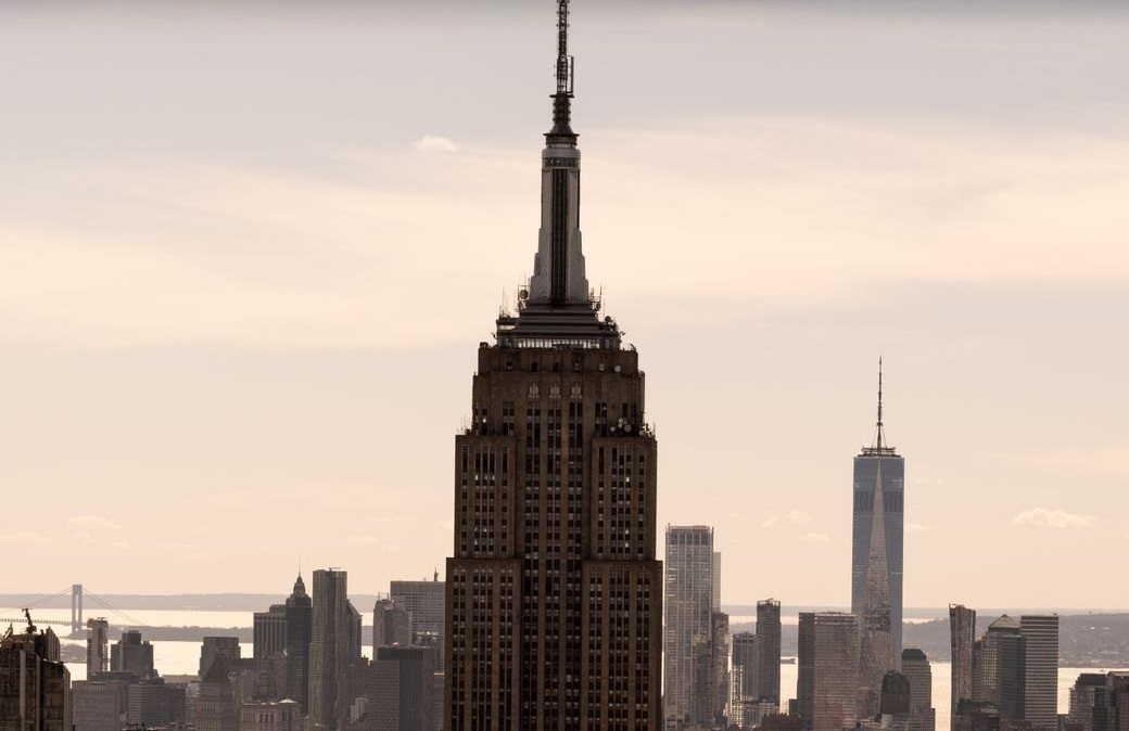 Empire State Building em primeiro plano, com os prédios do sul de Manhattan ao fundo, num céu de fim de tarde em tons de areia