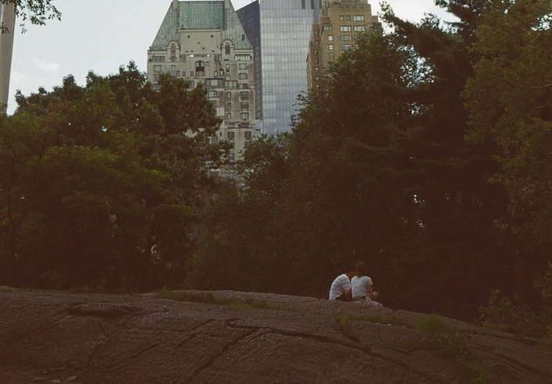 Árvores do Central Park com prédios de Manhattan ao fundo e duas pessoas sentadas numa rocha em primeiro plano