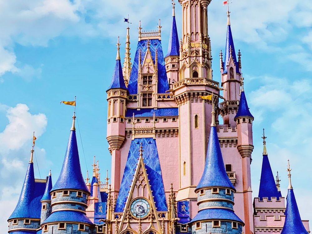 Torres azuis e cor-de-rosa do castelo do Magic Kingdom contra um céu azul com nuvens