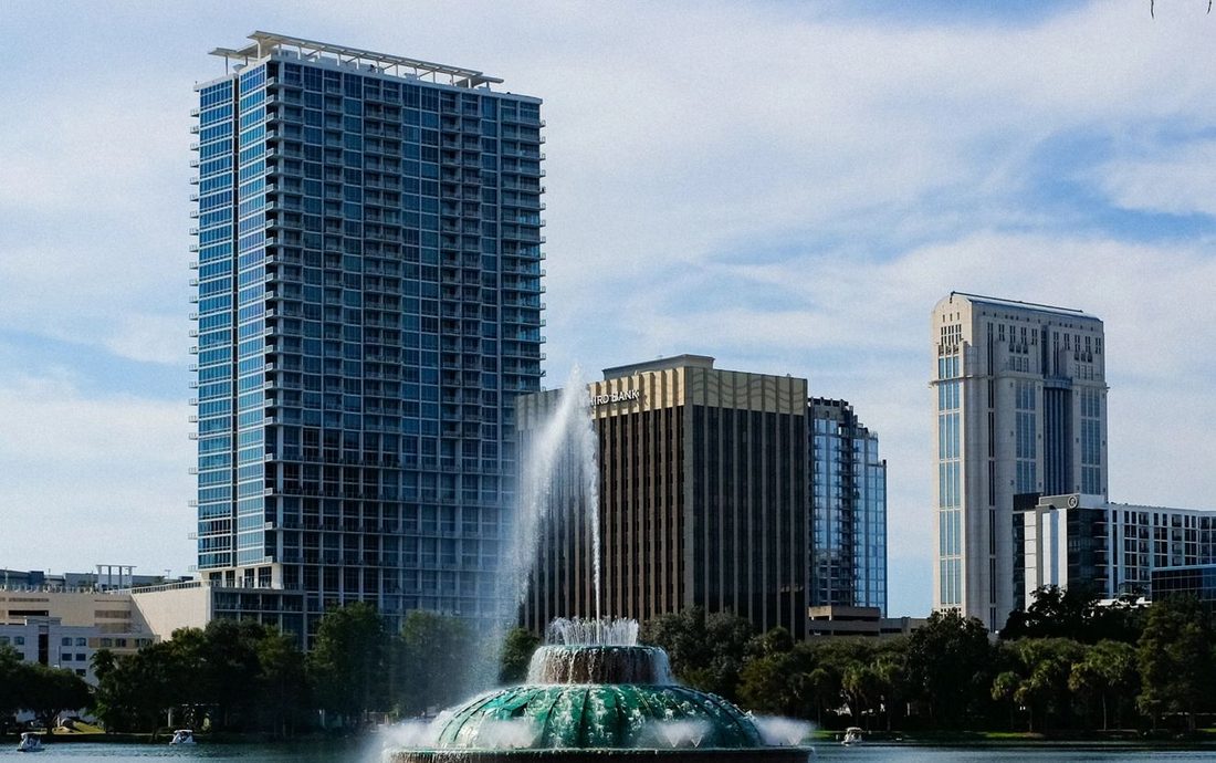 Prédios do centro de Orlando e a fonte do Lago Eola, com céu azul e nuvens