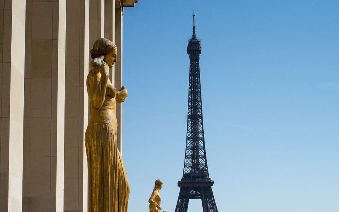 Torre Eiffel vista da esplanada do Trocadéro, com estátuas douradas em primeiro plano e céu azul
