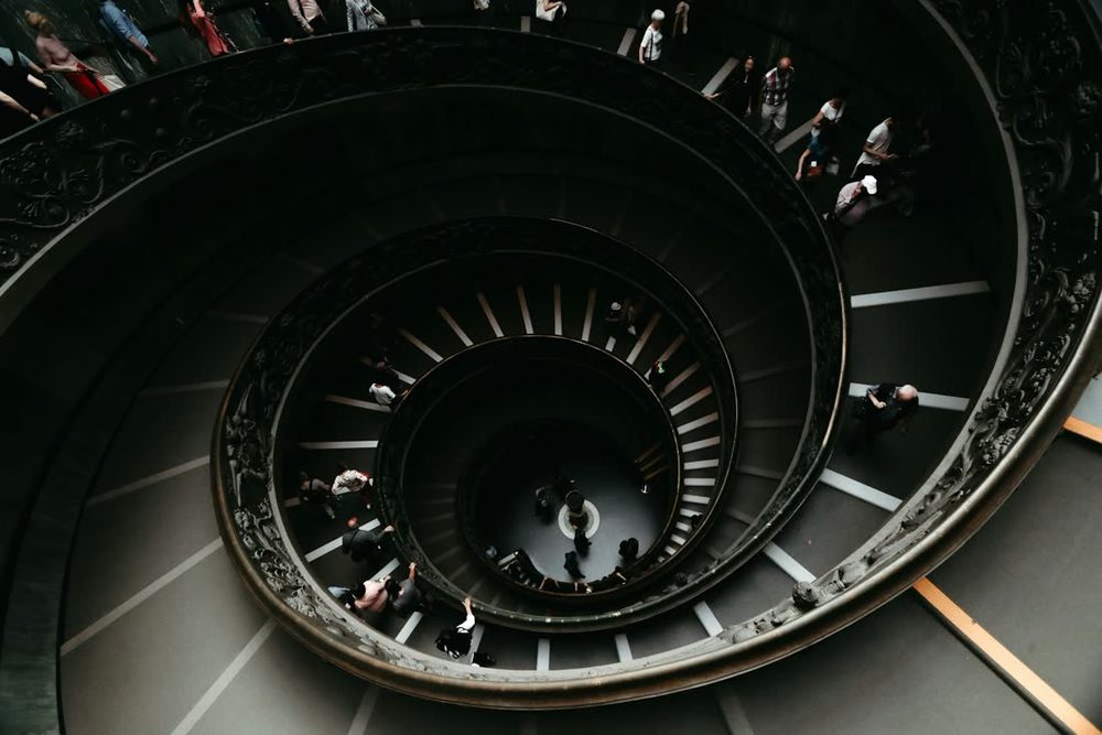 Escada em espiral dos Museus Vaticanos, vista de cima, com pessoas descendo os degraus