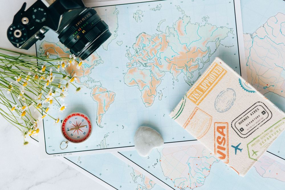 Mapa do mundo claro com câmera analógica, bússola, flores e caderno de carimbos de viagem