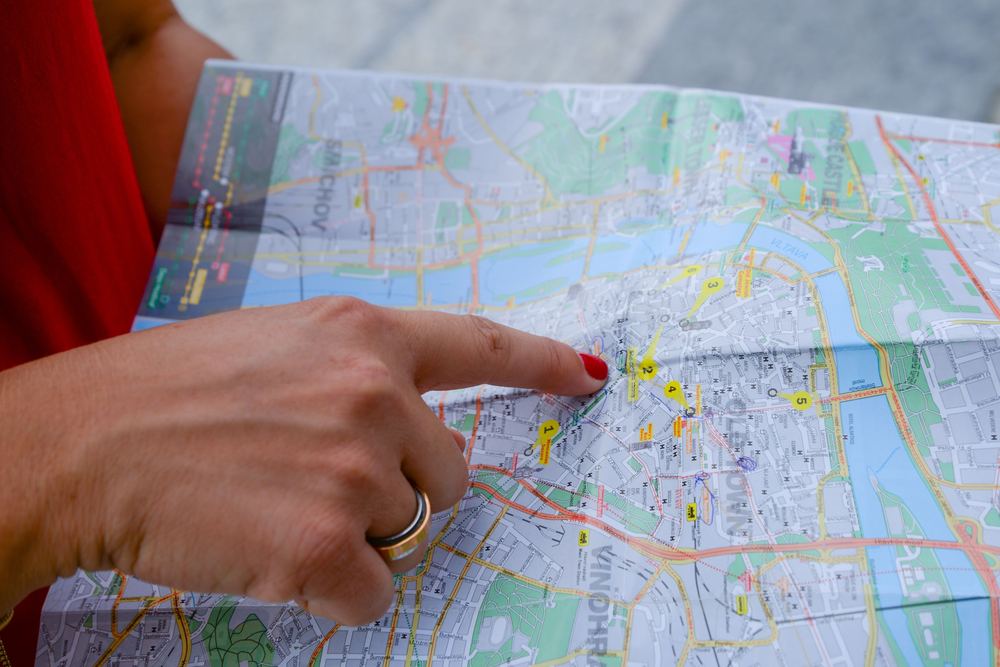 Dedo apontando um ponto em um mapa urbano de papel, com ruas e rio coloridos
