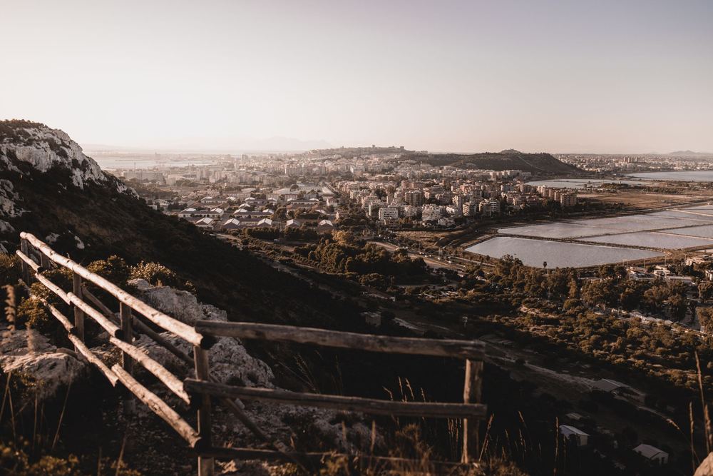 Mirante com cerca de madeira sobre a encosta, com cidade e lagoa ao fundo em luz dourada