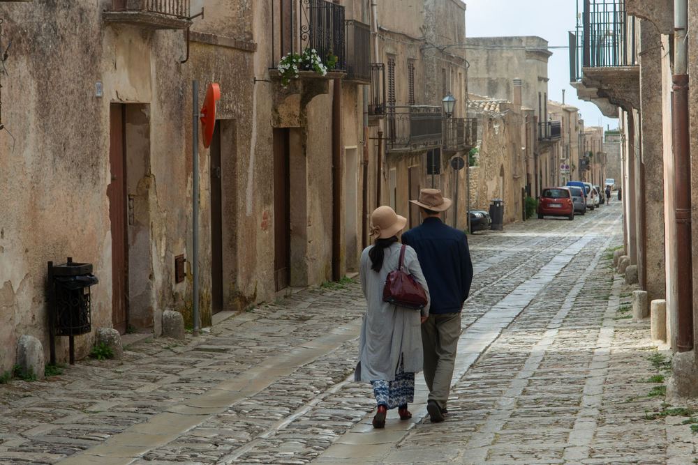 Casal caminhando por uma rua estreita de pedra entre casas antigas