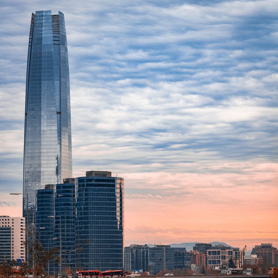 Torre de vidro da Costanera ao entardecer, com nuvens rosadas e outros prédios ao redor