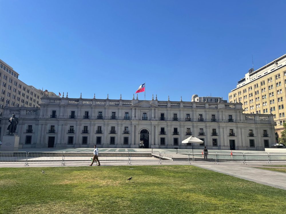 Fachada do Palácio de La Moneda, com a bandeira do Chile no alto e um gramado em primeiro plano