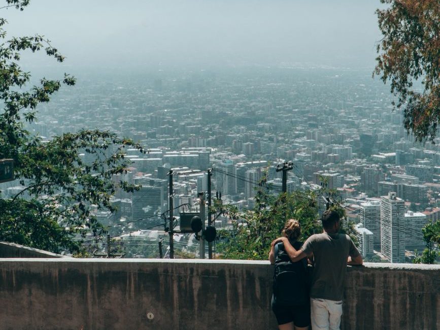 Casal abraçado olhando a cidade de Santiago, coberta por névoa, de um mirante do Cerro San Cristóbal