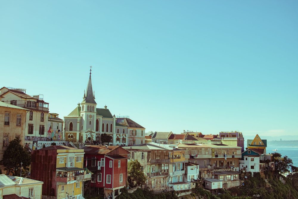 Casas coloridas de Valparaíso numa encosta, com uma igreja de torre pontuda e o mar ao fundo